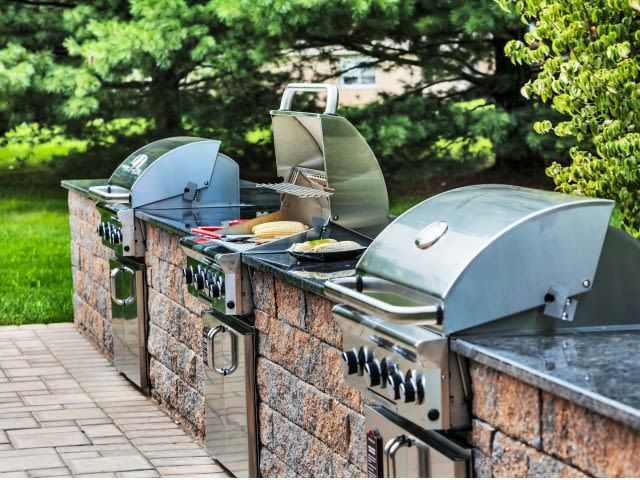 Outdoor communal grilling station with stainless steel gas grills built into a stone counter.