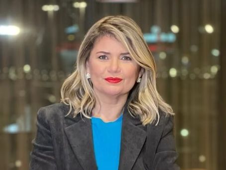 The woman is wearing a blue shirt and a gray jacket.
