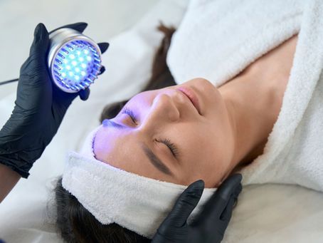 A woman is getting a blue light treatment on her face.
