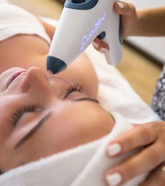 A technician uses a handheld CoolSculpting device on a person’s face while they lie on a treatment table.