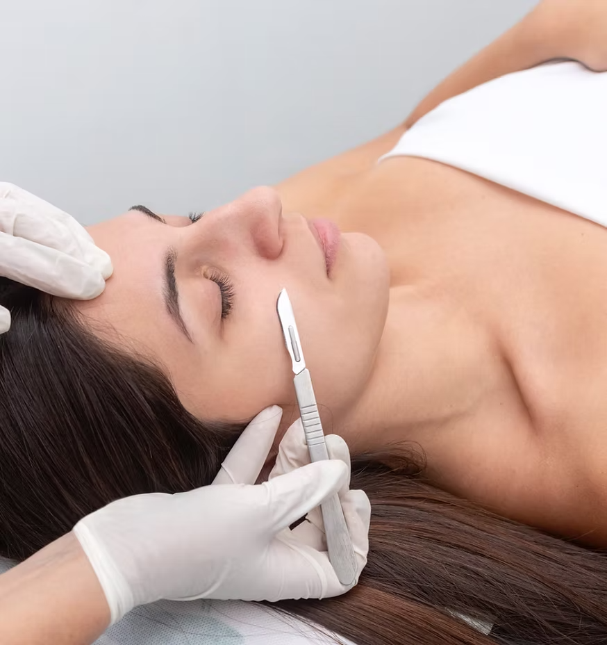 A person receives a dermaplaning facial treatment with a scalpel while lying on an exam table.
