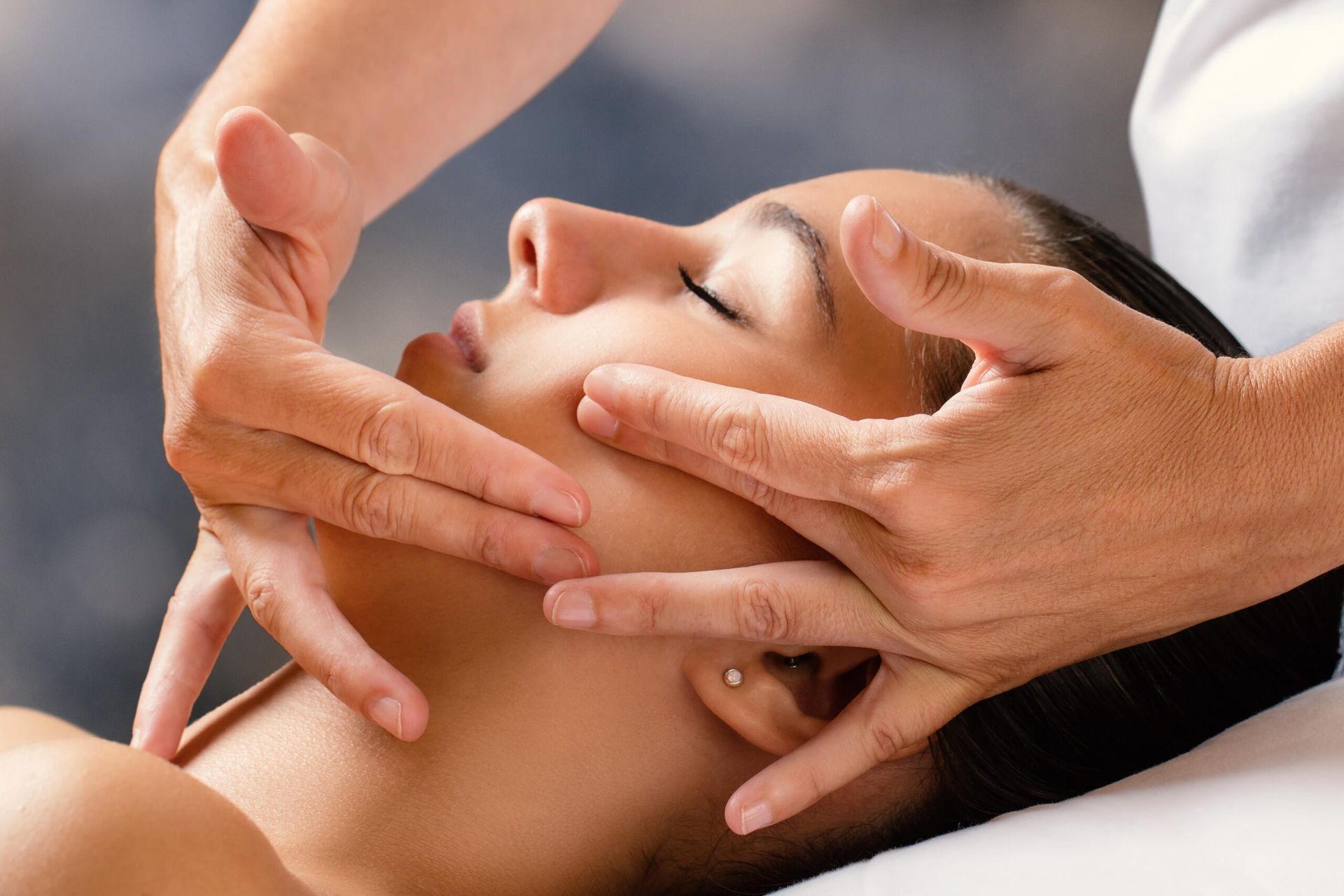 A person receiving a professional facial massage, with hands gently touching the cheek and jawline.
