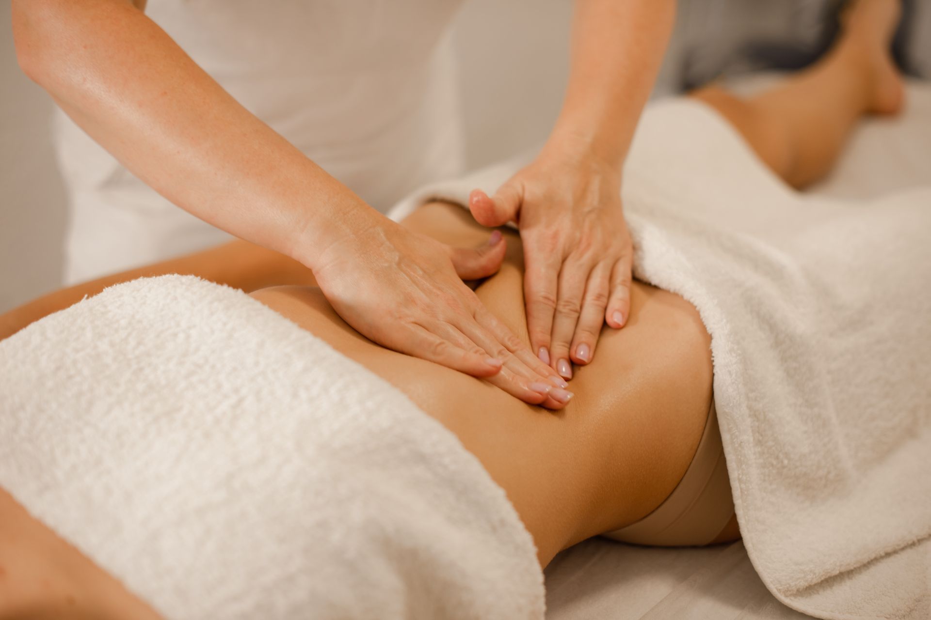 A massage therapist performing an abdominal massage on a person lying on a massage table covered with white towels.