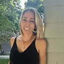 A woman in a black tank top is smiling while leaning against a wall.