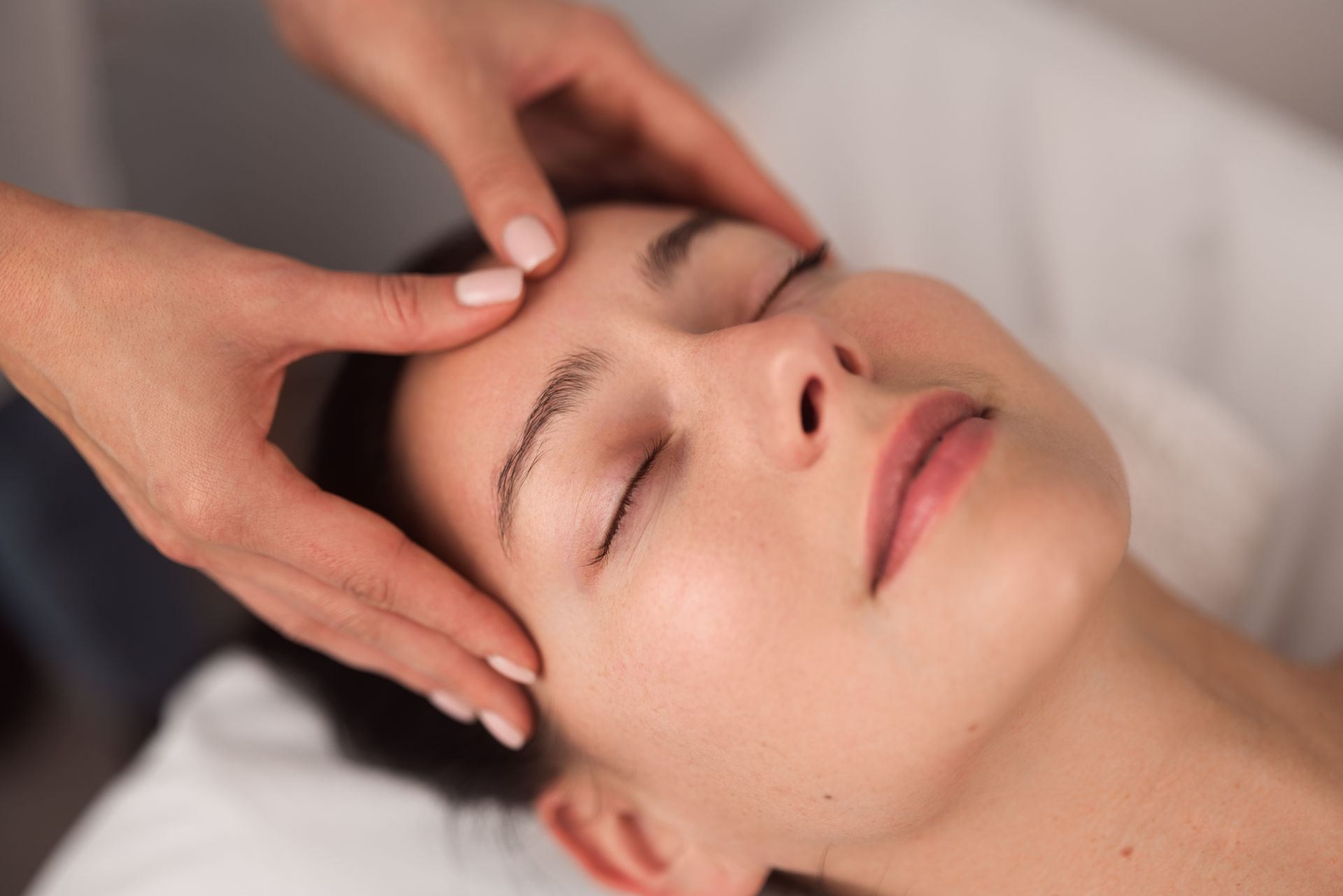 A person receiving a relaxing facial massage, with hands gently pressing on their forehead.