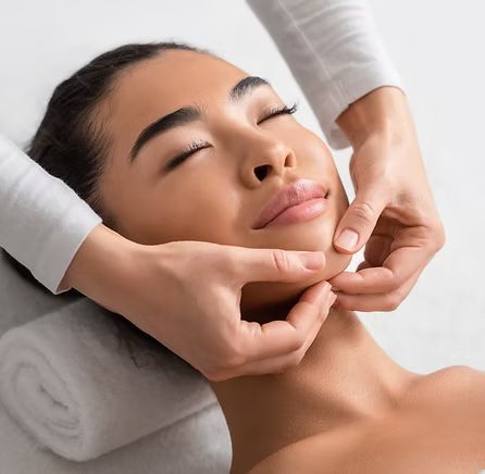 A person receiving a relaxing facial massage, with eyes closed, lying on a white towel.