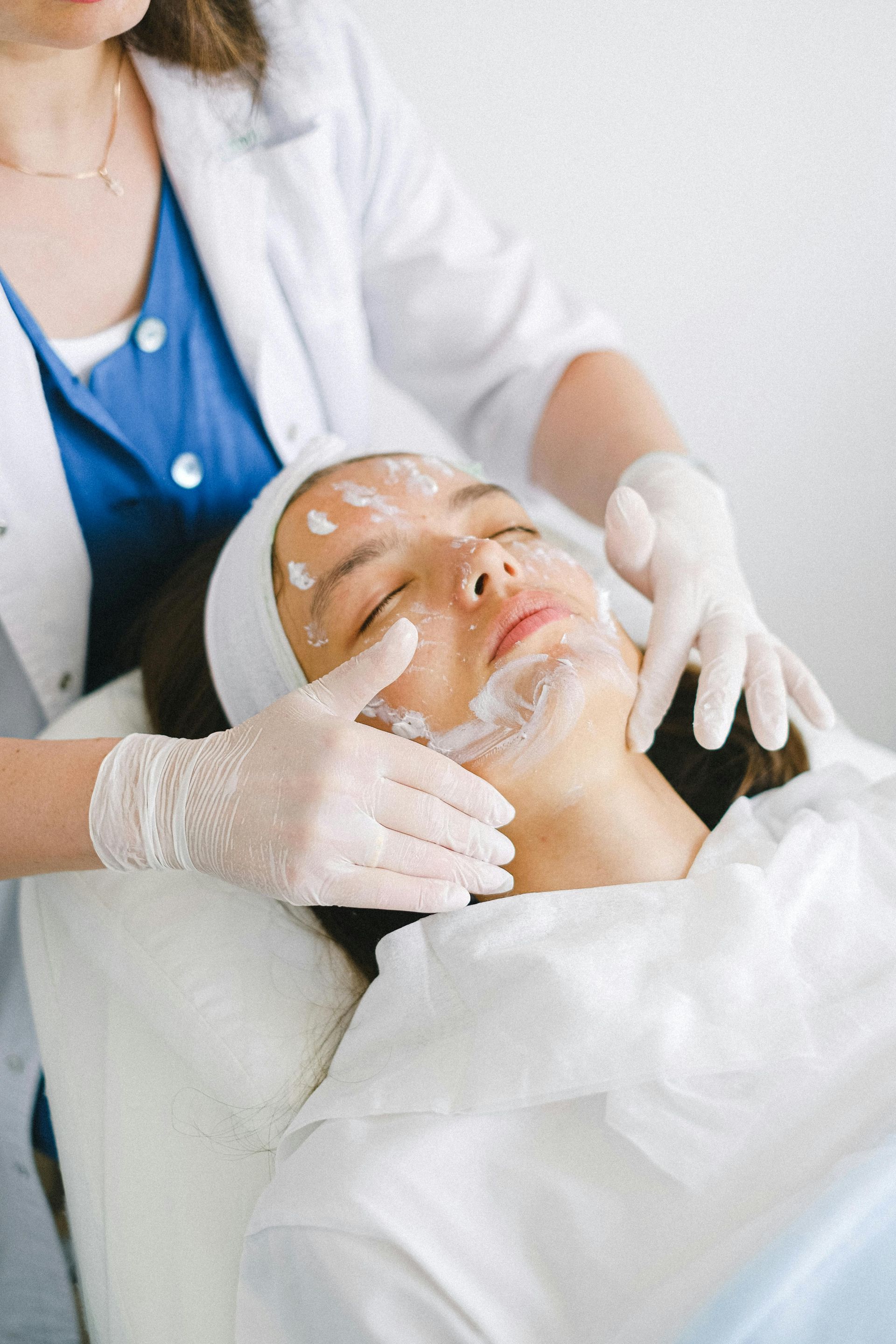 A person wearing gloves applies white cream to a client's face during a spa treatment.