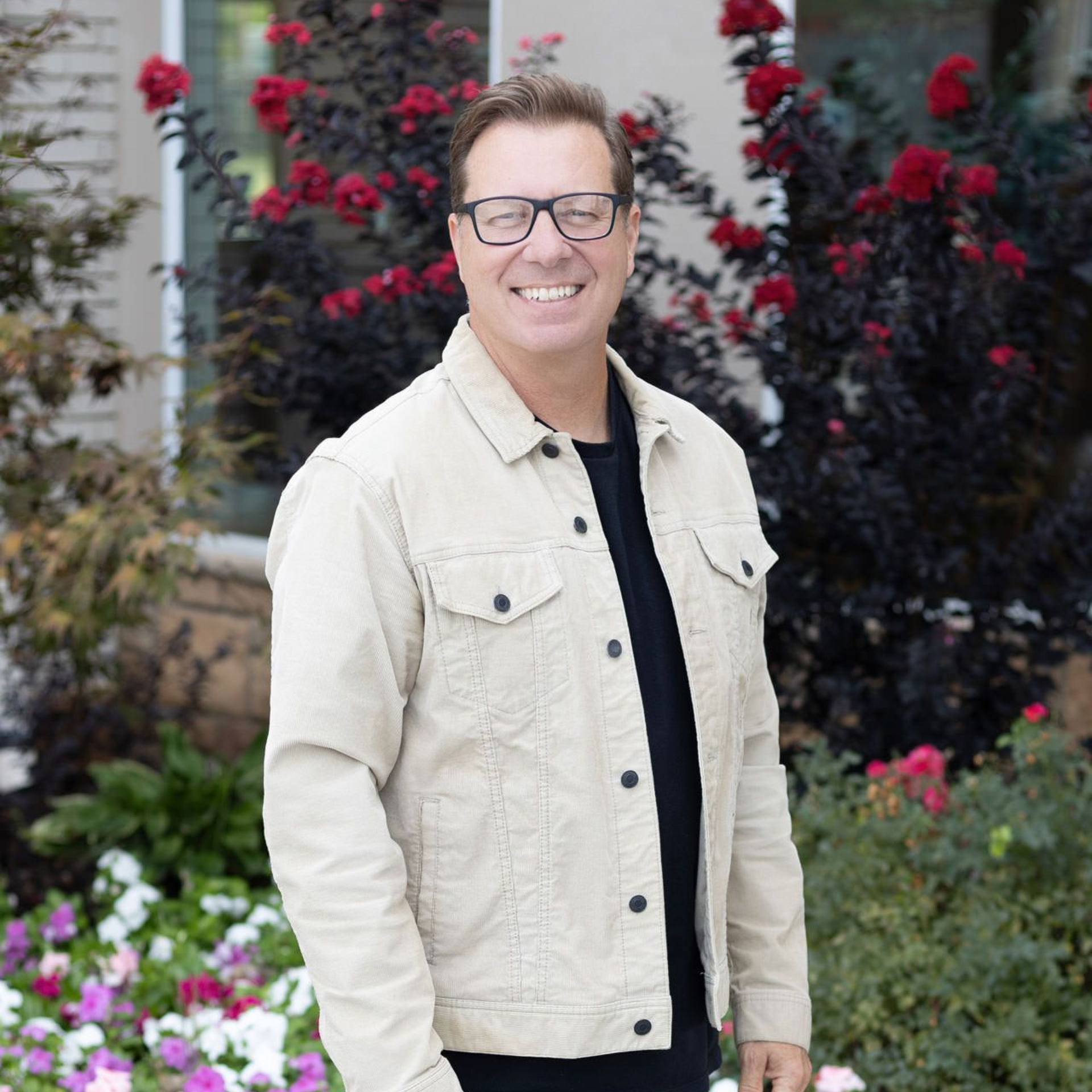 A man wearing glasses is smiling with his arms crossed