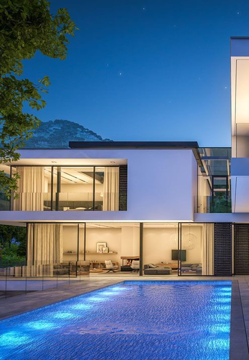 A modern house with a swimming pool in front of it at night.