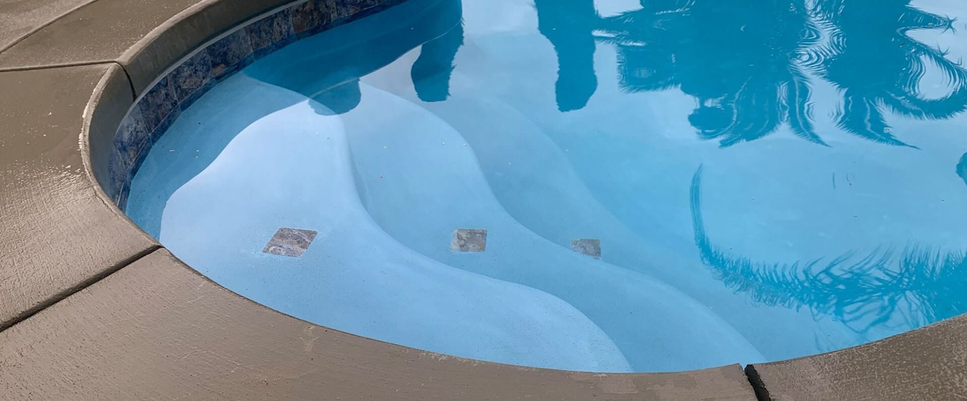 A person is standing in a swimming pool with their reflection in the water.