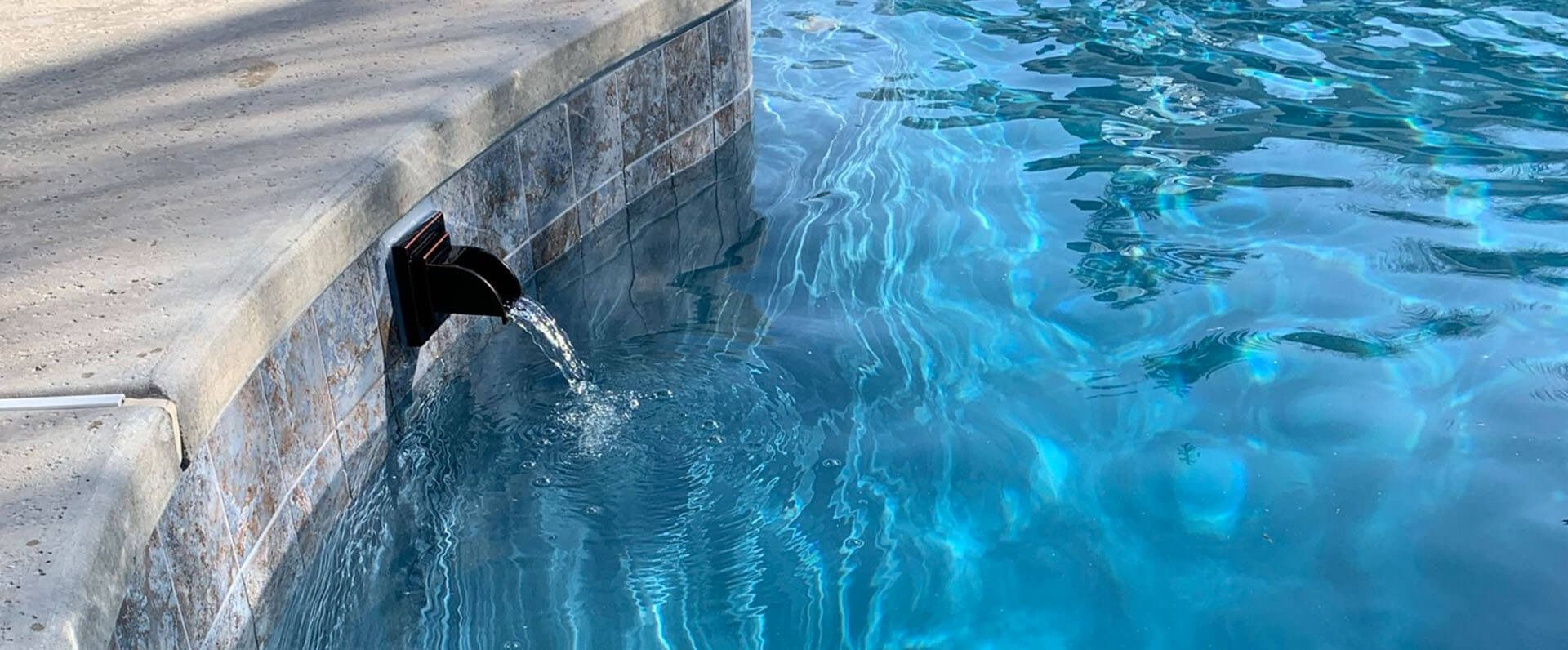 A waterfall is coming out of the side of a swimming pool.