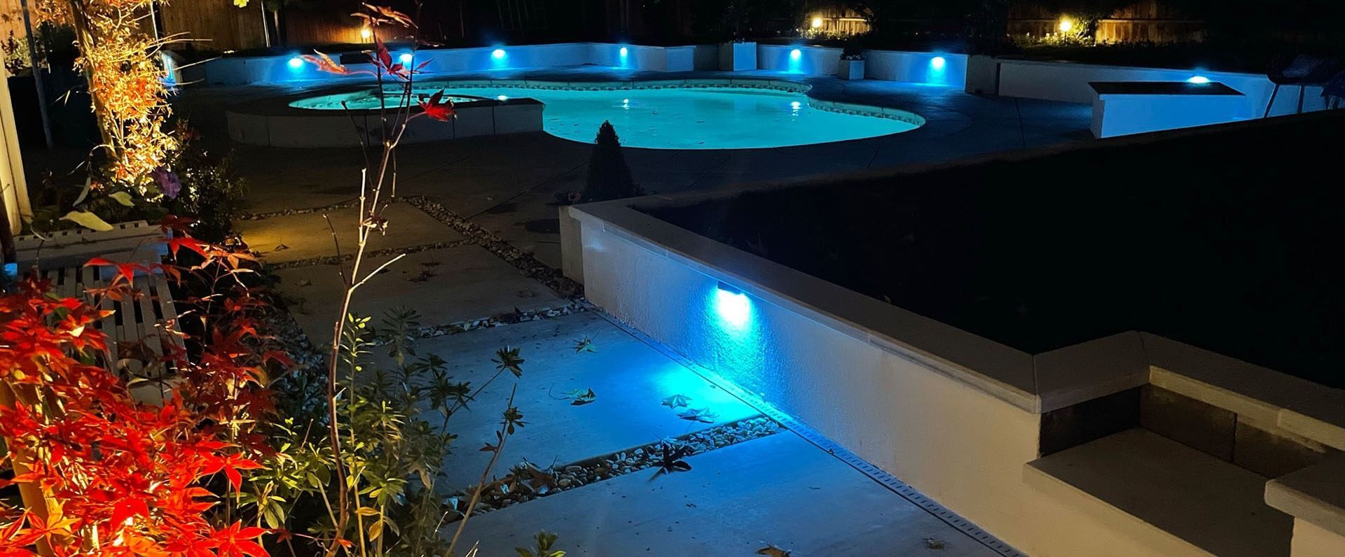 A large swimming pool is lit up at night with blue lights.