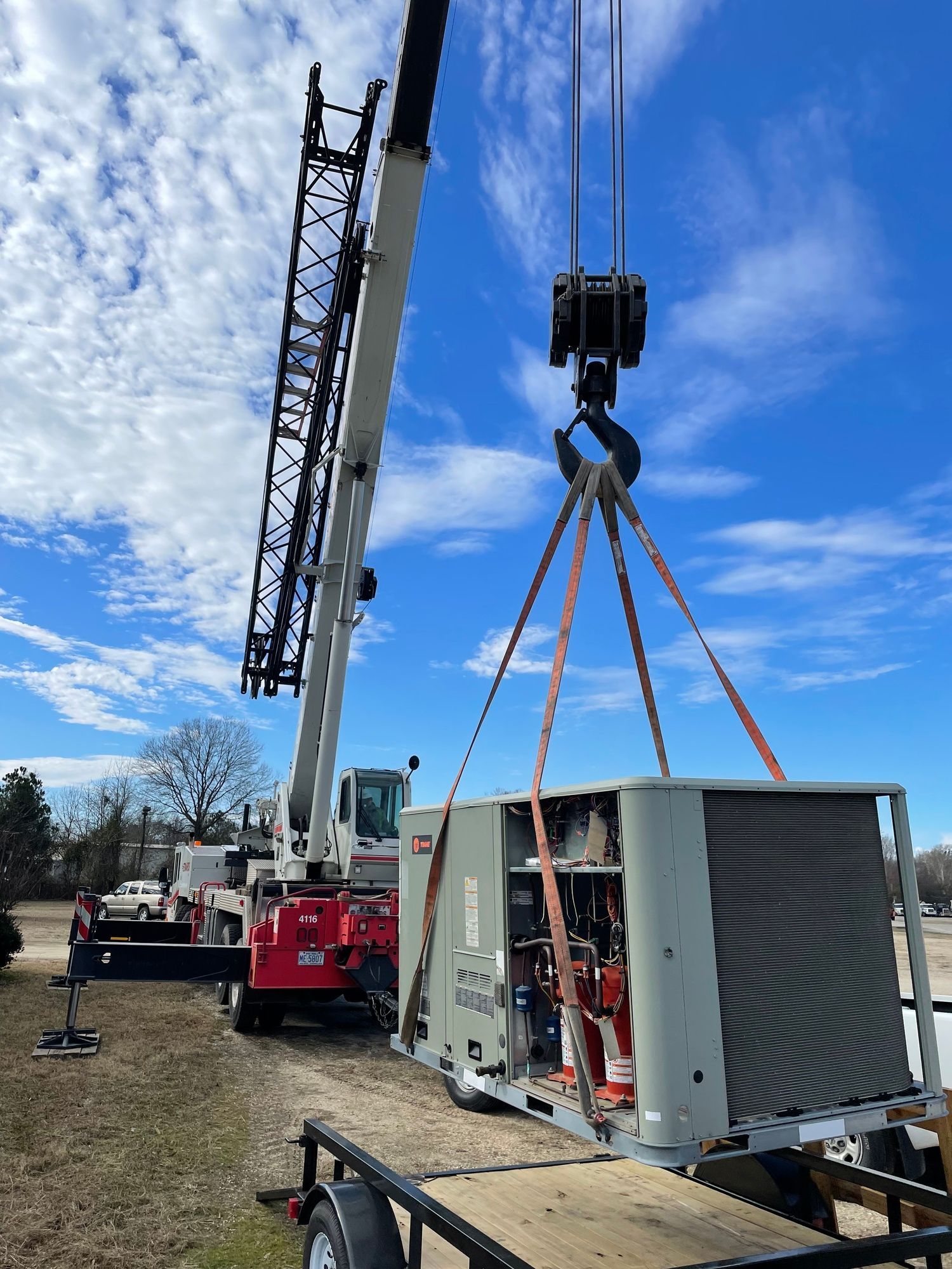 A crane is lifting a large piece of equipment over a trailer.