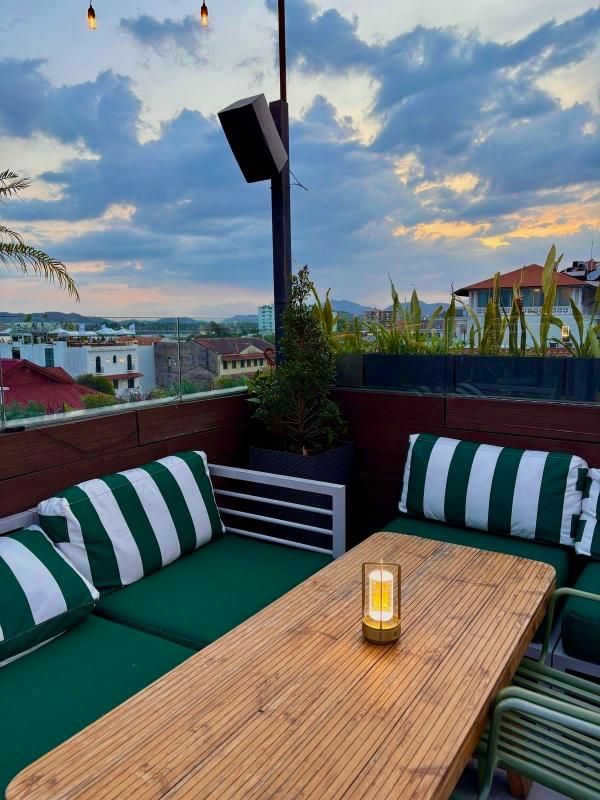 Salón en la azotea con cojines de rayas verdes y blancas, mesa de madera y cielo nocturno de fondo.