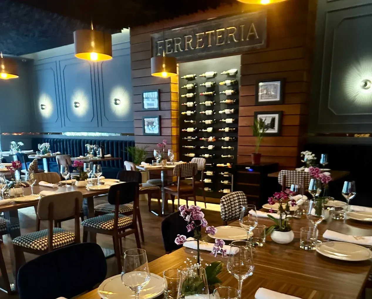 Interior de restaurante con mesas puestas, botellero y cartel de 