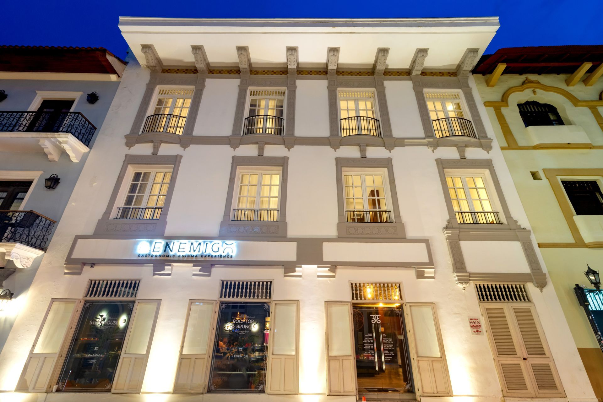 Edificio blanco de tres pisos con molduras grises, ventanas y un letrero que dice 