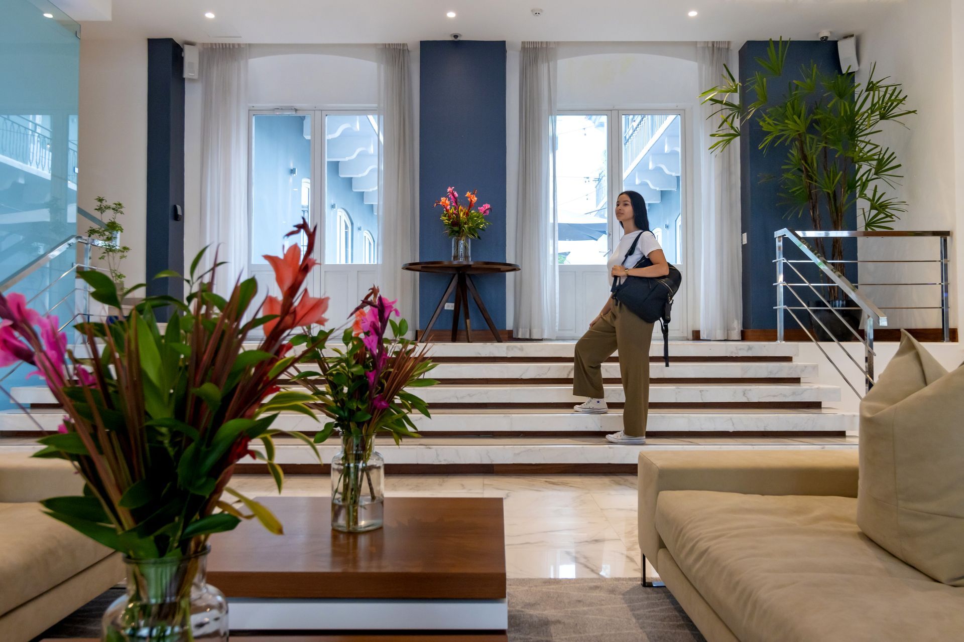 Una mujer con mochila sube las escaleras en un vestíbulo moderno con flores y sofás.