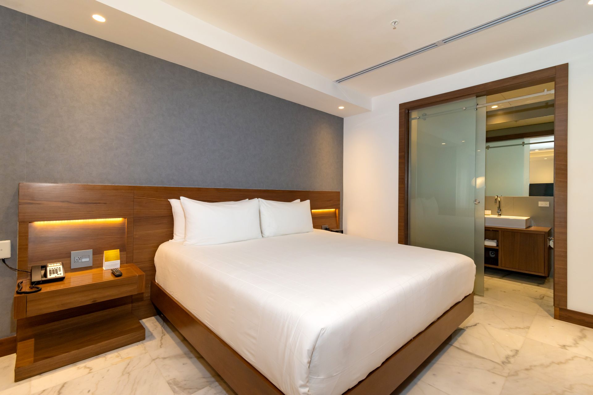 Habitación de hotel con cama, mesita de noche y puerta de cristal al baño.