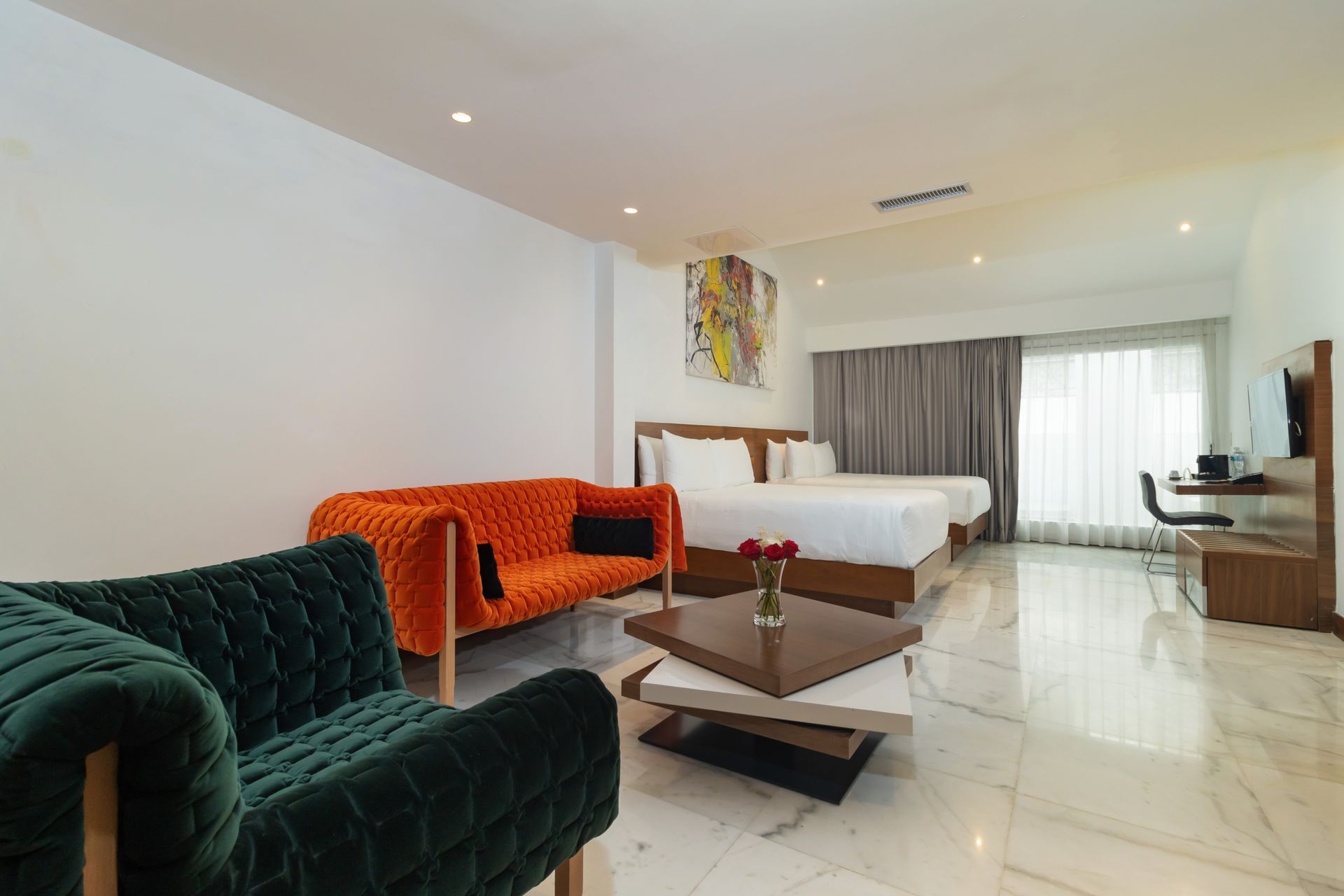 Suite de hotel con sofá naranja, sillón verde, cama doble y decoración moderna.