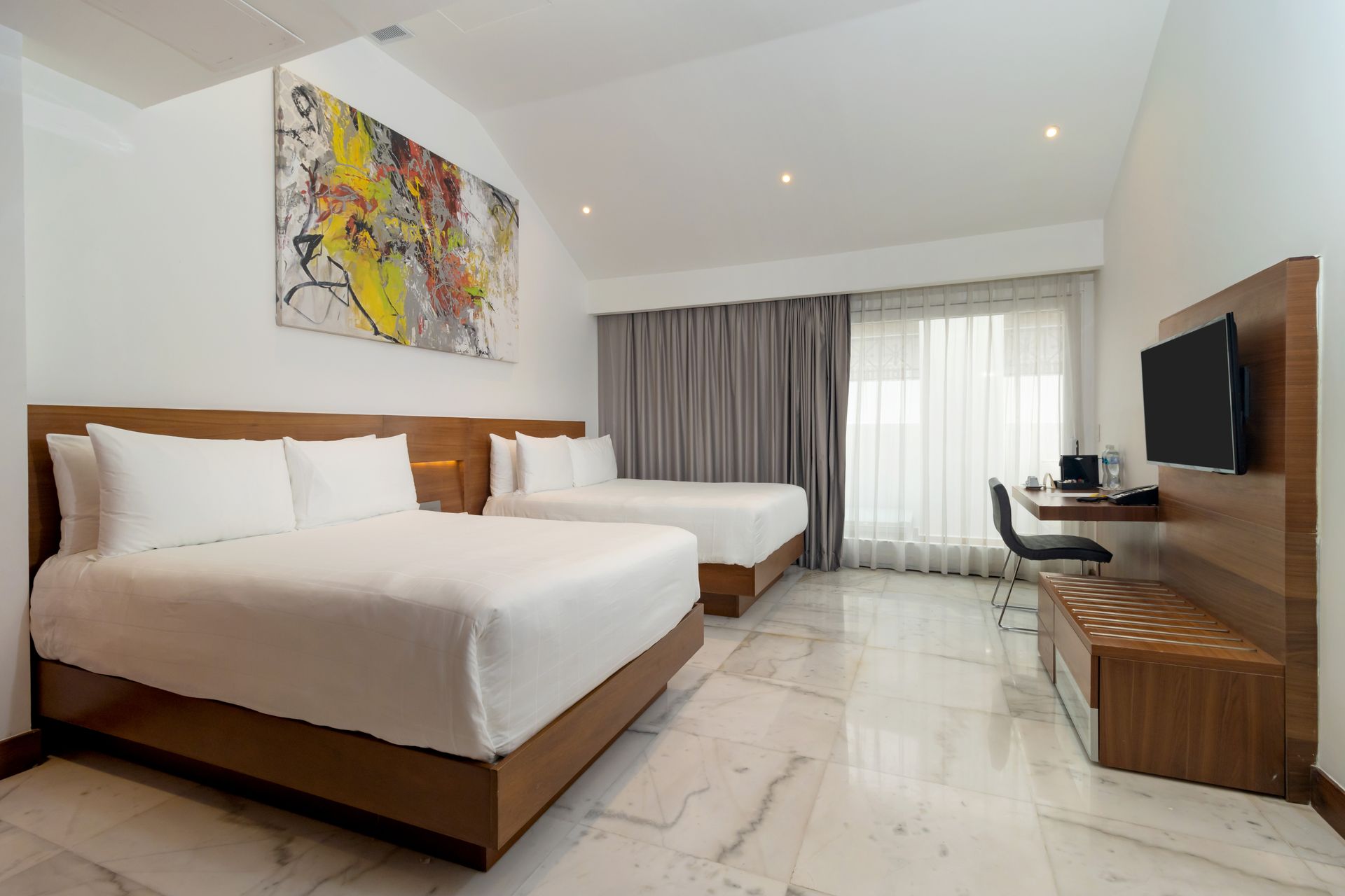Habitación de hotel con dos camas, escritorio y una gran obra de arte abstracto sobre una pared blanca.
