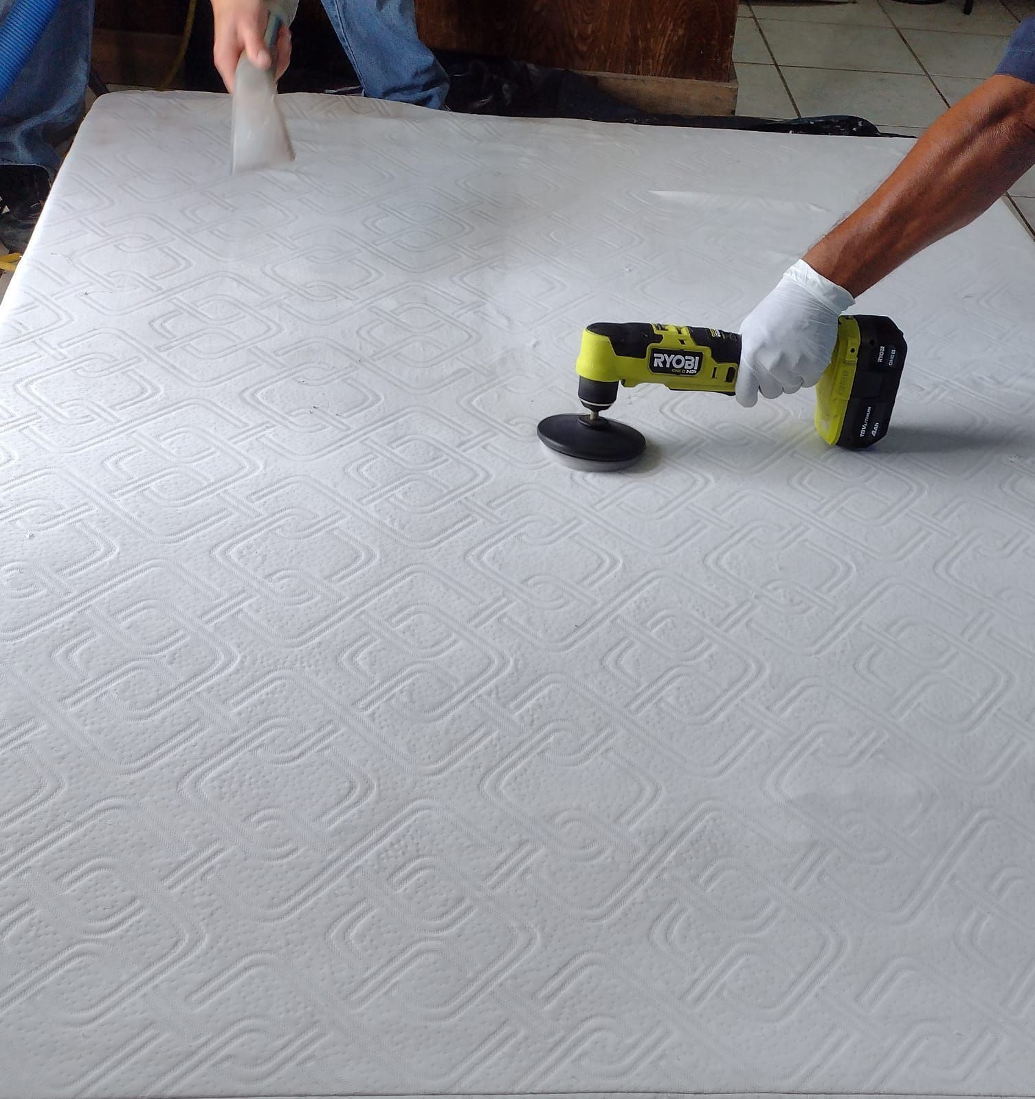 Una persona usa una herramienta eléctrica de mano sobre un colchón. Otra persona usa un raspador.