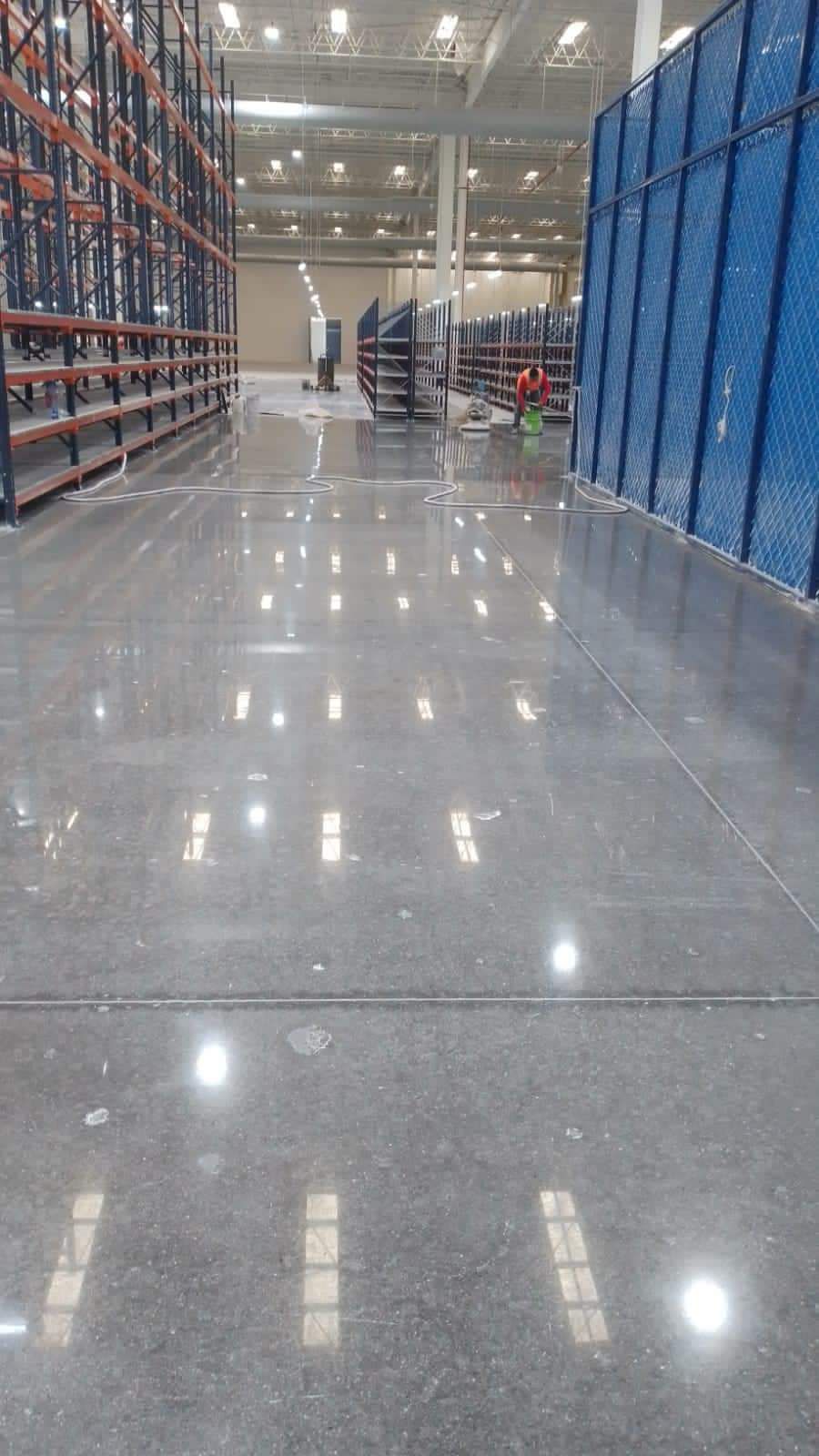 Interior de almacén con suelo de hormigón pulido, estanterías y barrera de seguridad azul.