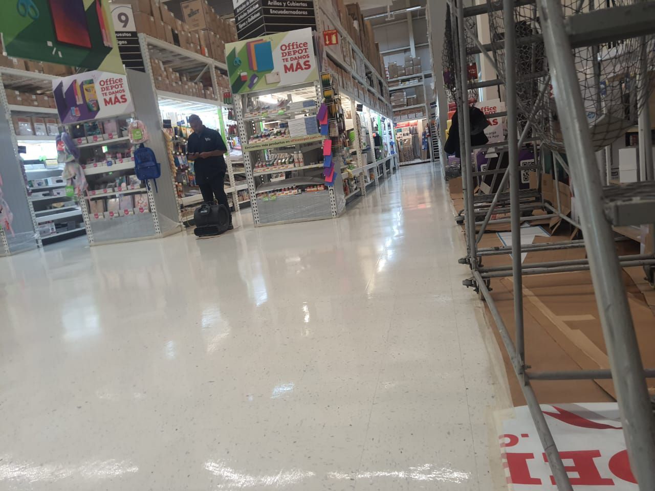 Pasillo bien iluminado de una tienda con una persona vestida de negro caminando. Estantes repletos de artículos.
