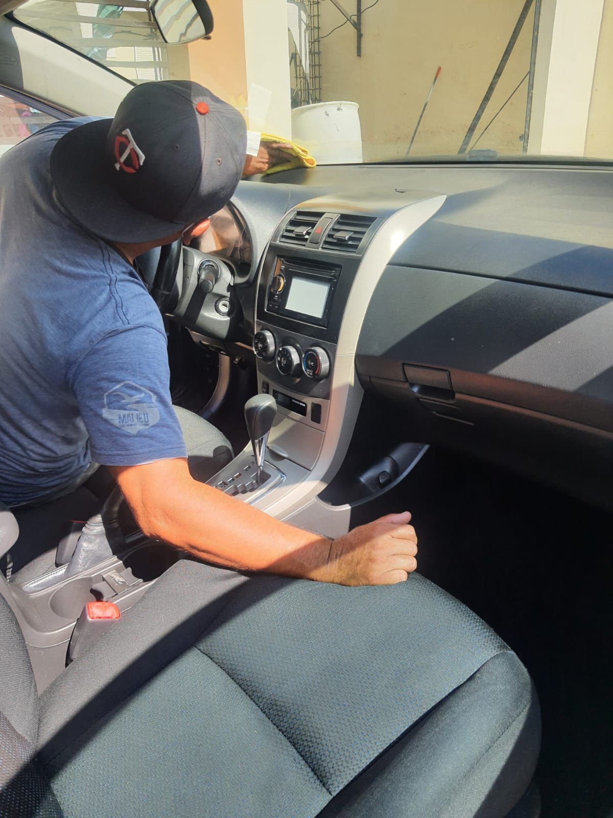 Hombre limpiando el interior de un coche; se ven el tablero, los asientos y el volante.