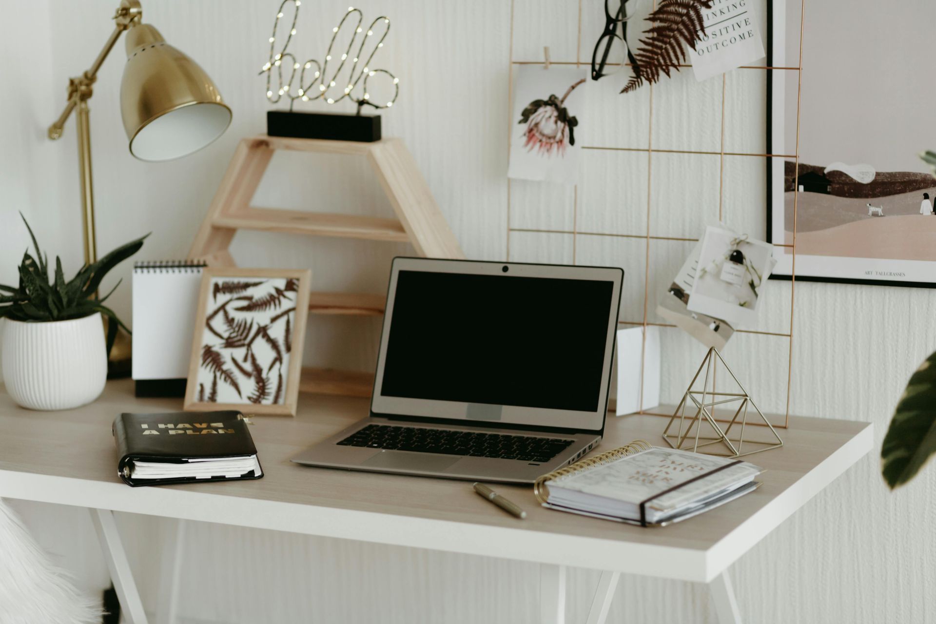 Minimalist white desk with laptop, lamp, plants, books, and framed art in a cozy home workspace