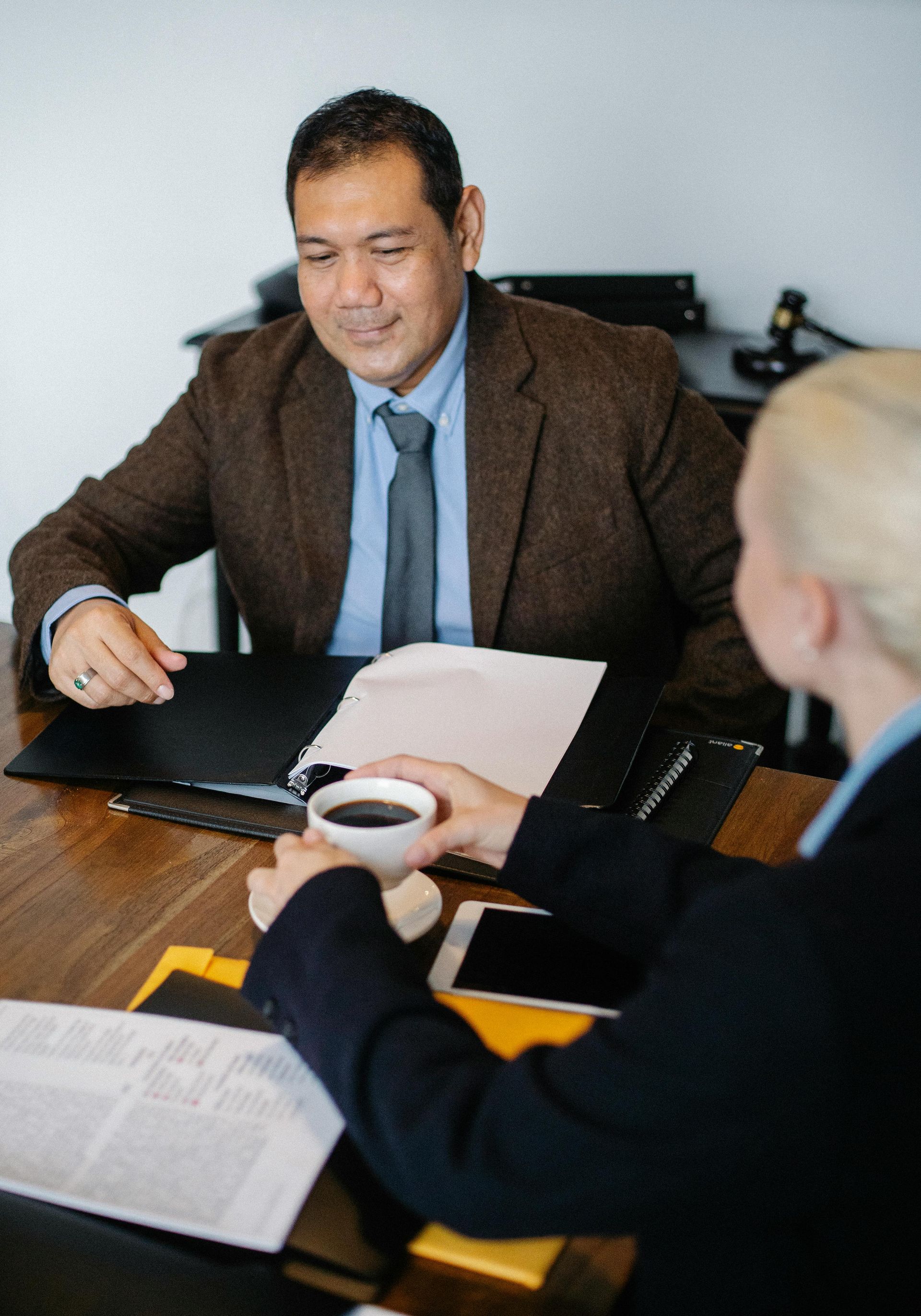 Two people discuss documents at a conference table, one holding a coffee cup.