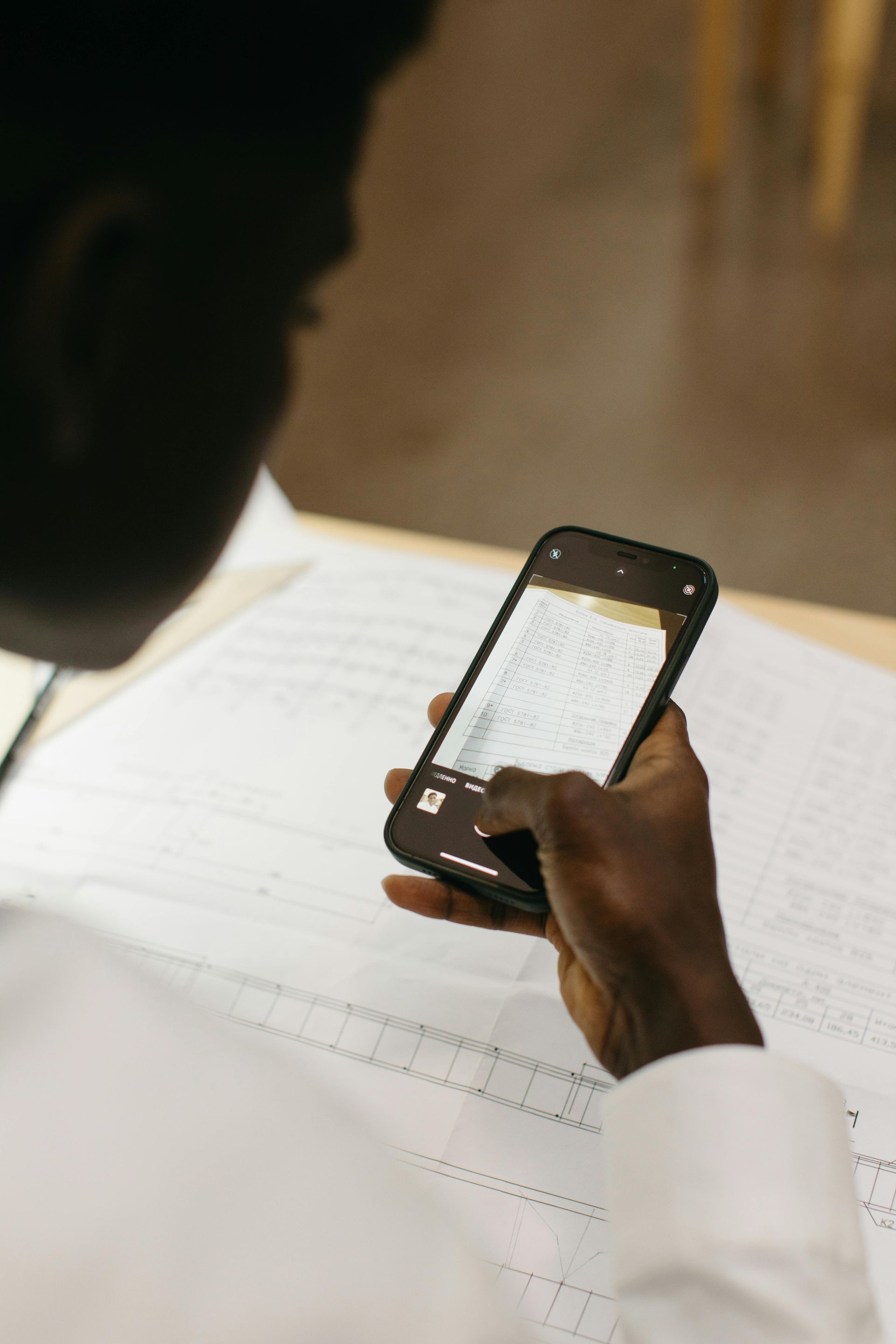 Person holds a smartphone over a notebook, viewing notes in a dimly lit setting.