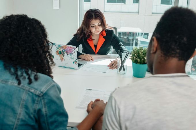 Job interview at a desk with three people, documents, laptop, and a small plant in a bright office.