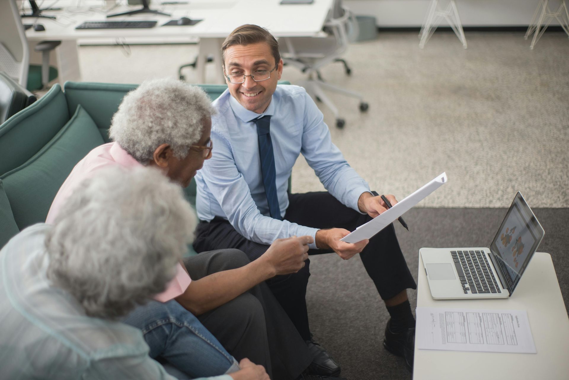 Three coworkers in a meeting, smiling and reviewing papers beside a laptop in a bright office