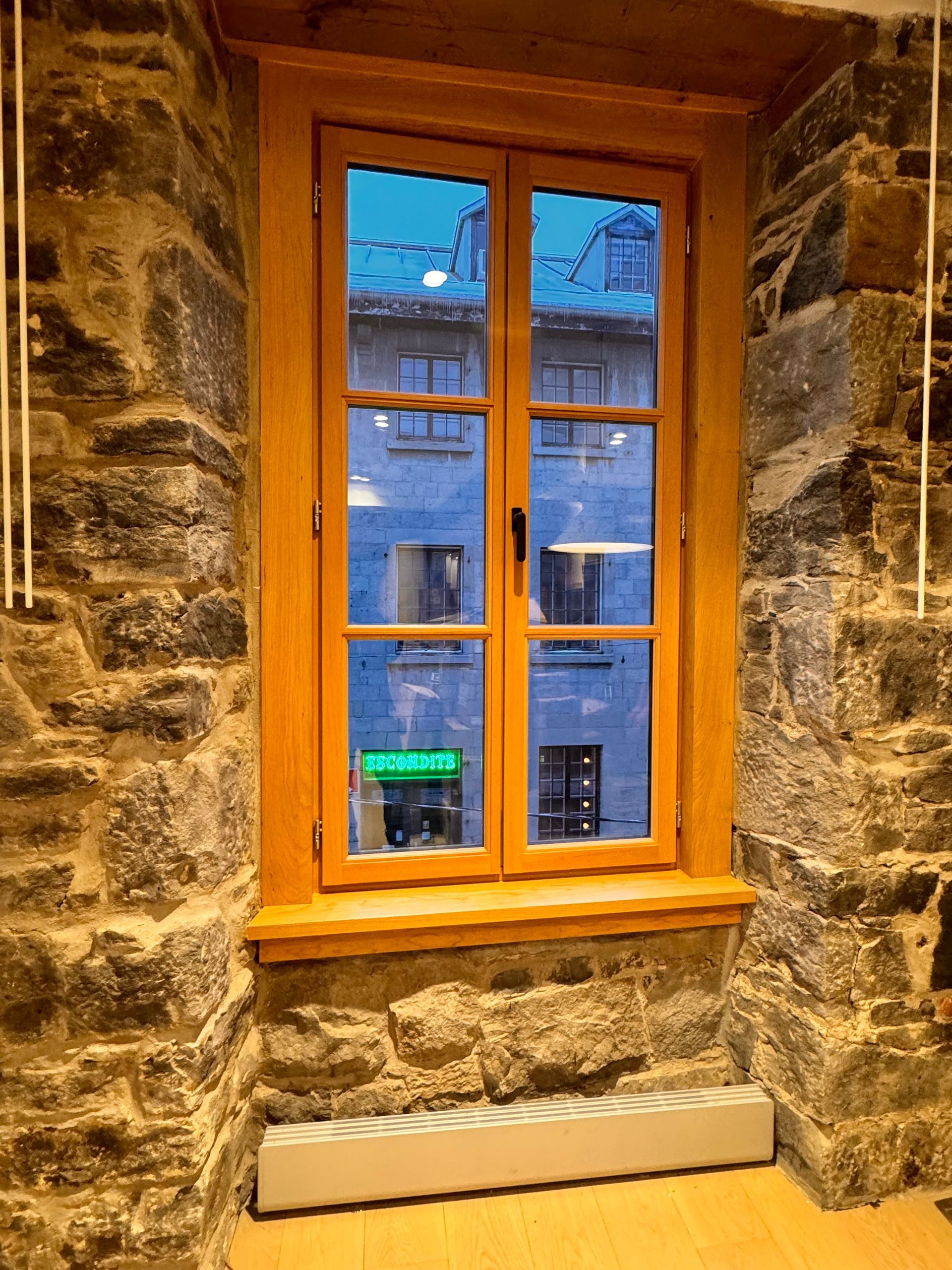 Fenêtre en bois dans un mur de pierre, reflétant une rue de la ville. Un radiateur se trouve en dessous.
