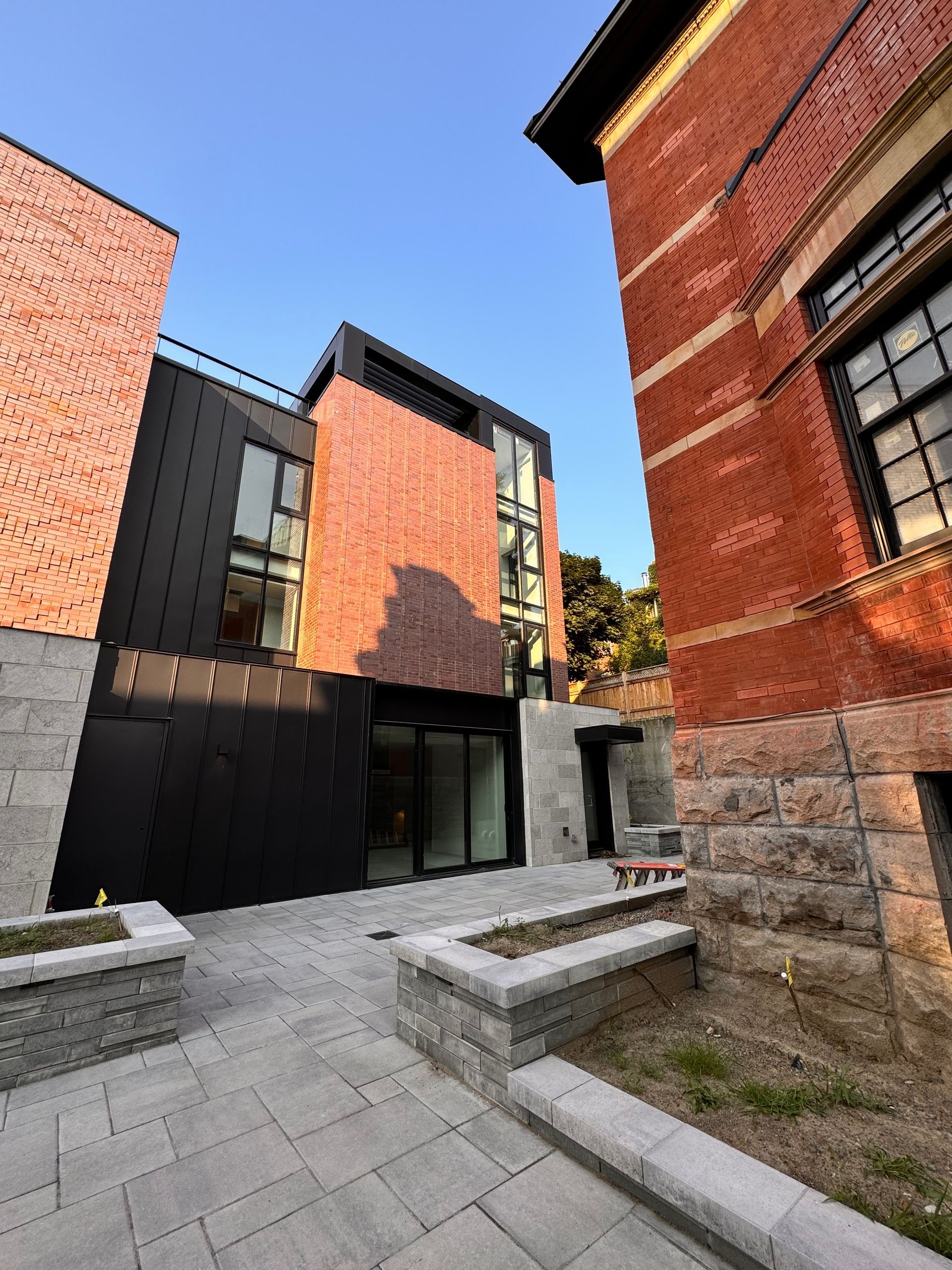 Bâtiment moderne en briques noires avec un bâtiment en briques plus ancien adjacent, ciel bleu.