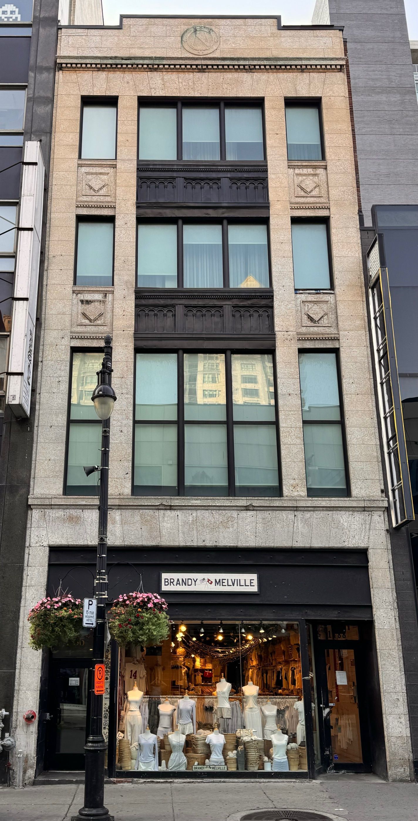 Un immeuble haut et étroit avec une boutique au rez-de-chaussée. Façade beige, encadrements de fenêtres foncés et éléments décoratifs.