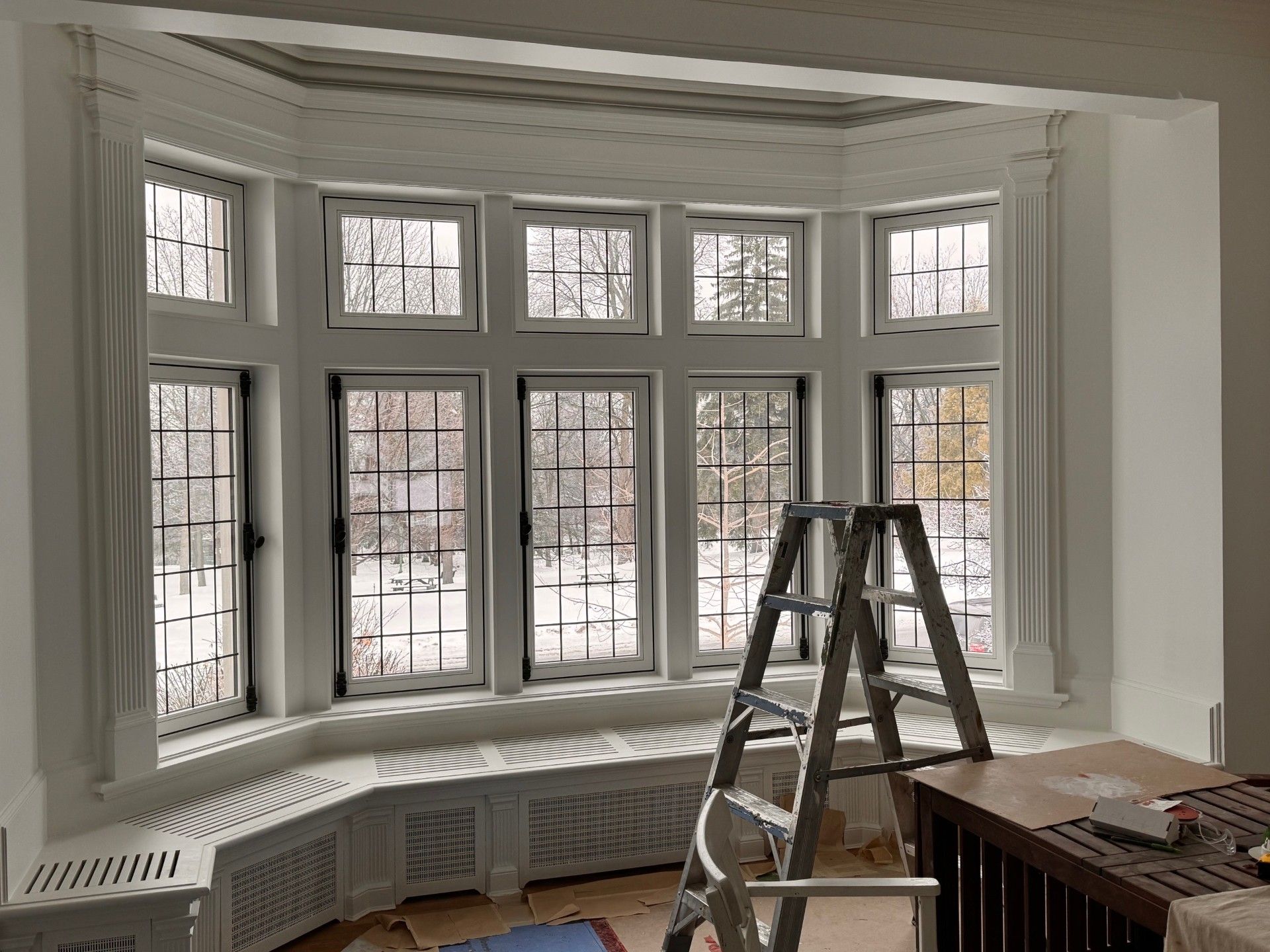 A ladder is sitting in front of a bay window in a room.