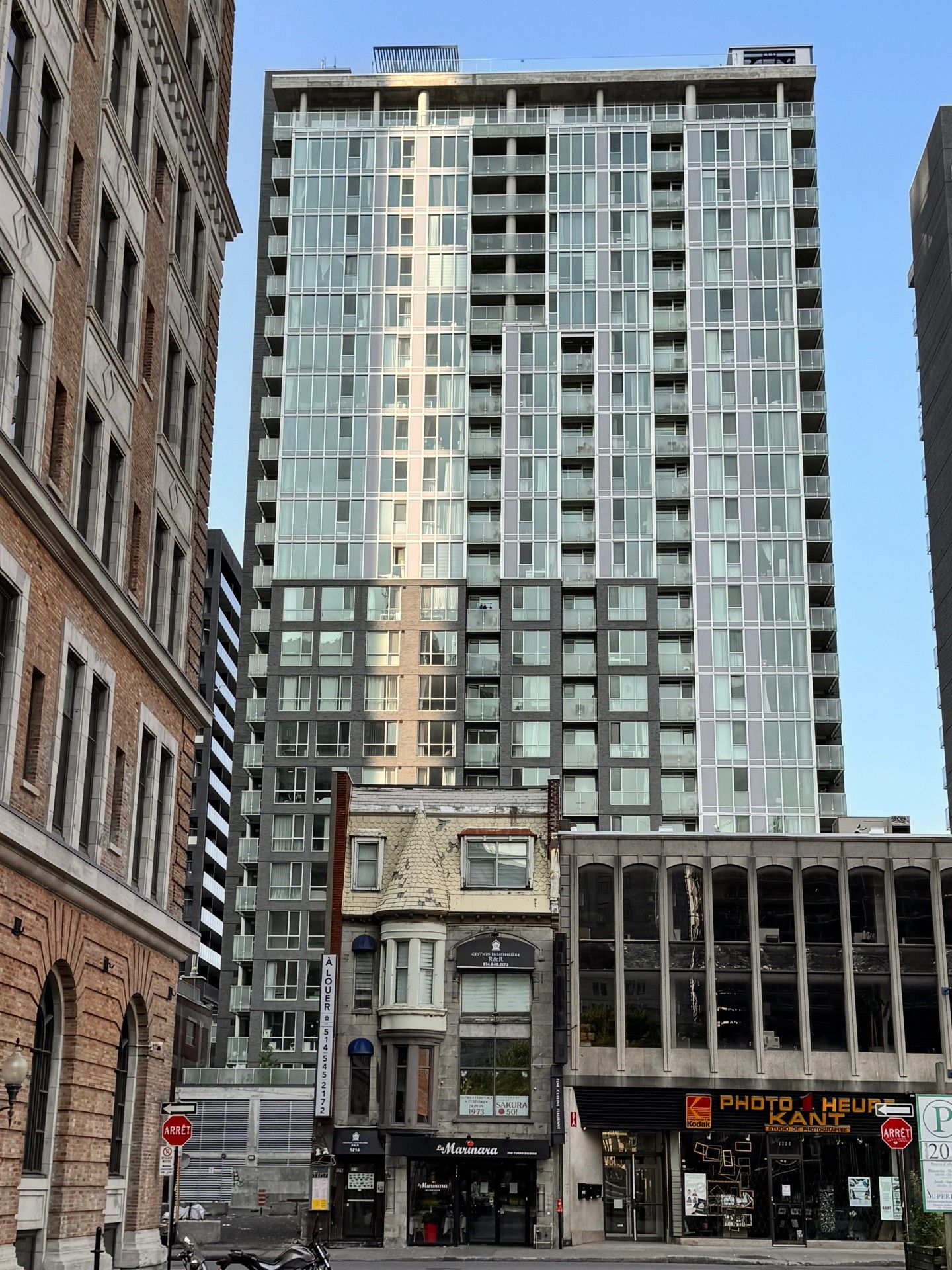 Un gratte-ciel moderne et imposant domine des bâtiments plus petits et plus anciens dans une rue de la ville.
