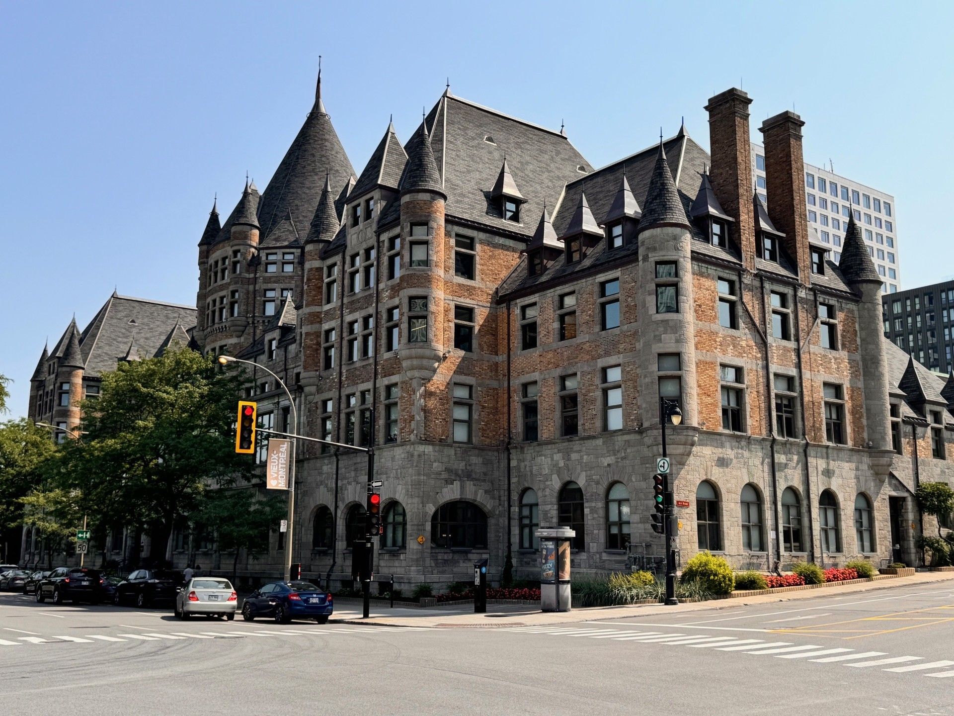 Bâtiment en pierre de style gothique avec tourelles et cheminées à un coin de rue, ciel bleu.