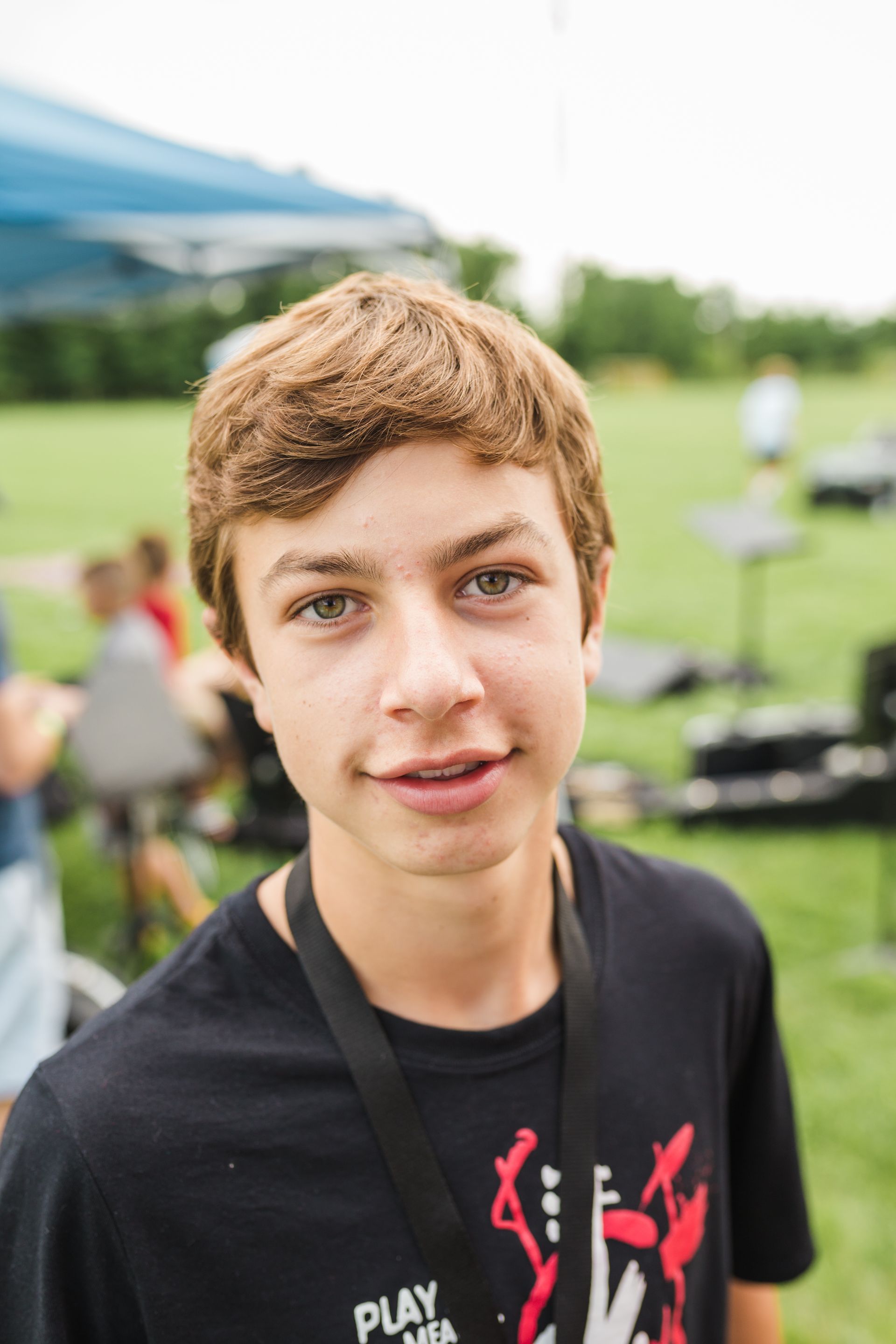 A young boy wearing a black shirt and a lanyard is standing in a field.