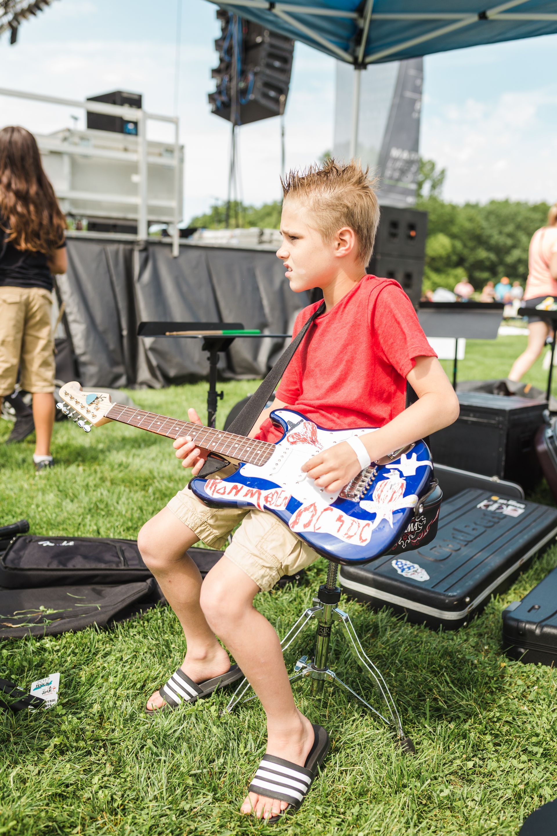 A young boy is sitting on a chair playing an electric guitar.