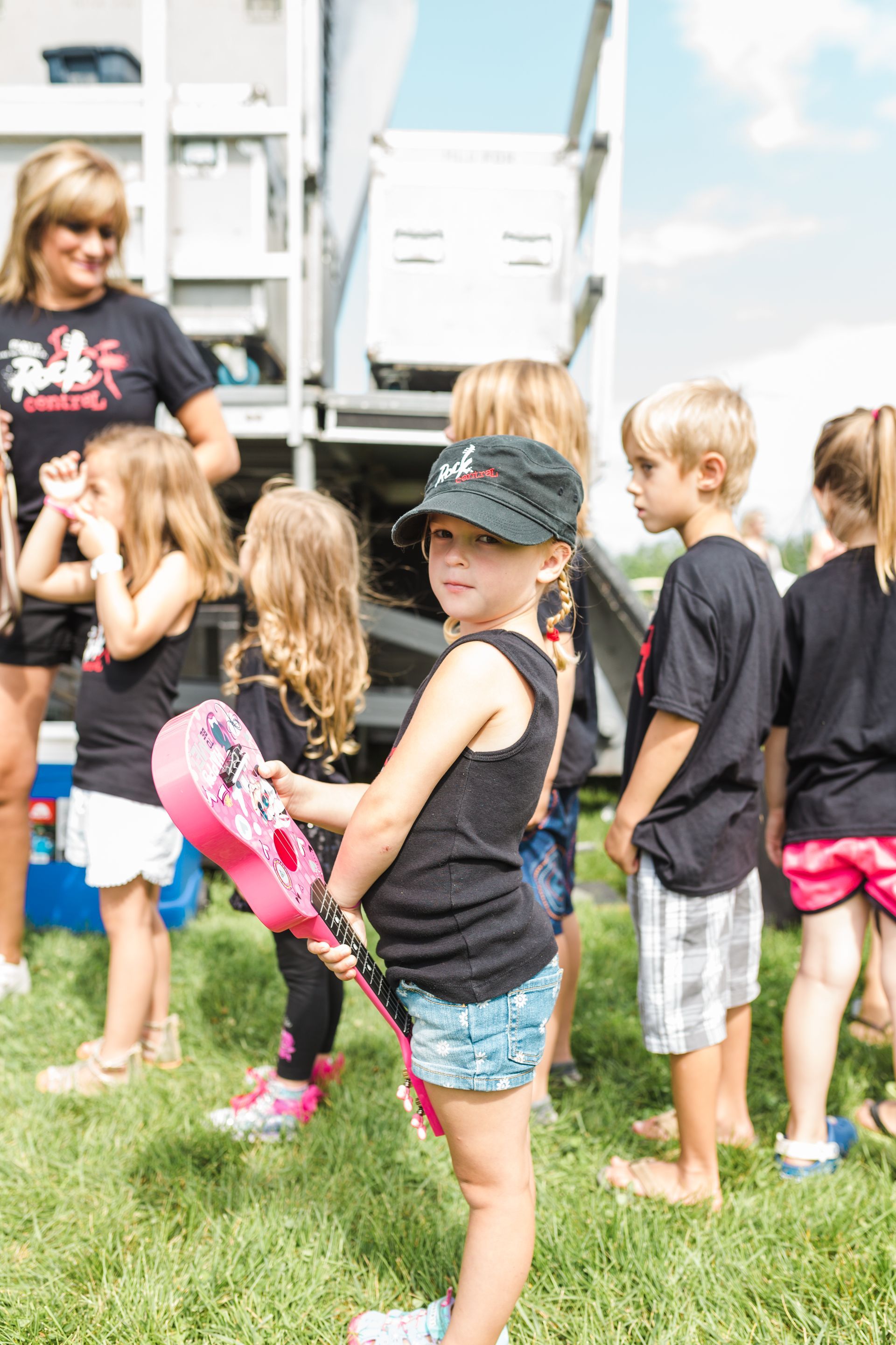 A group of children are standing in the grass holding guitars.