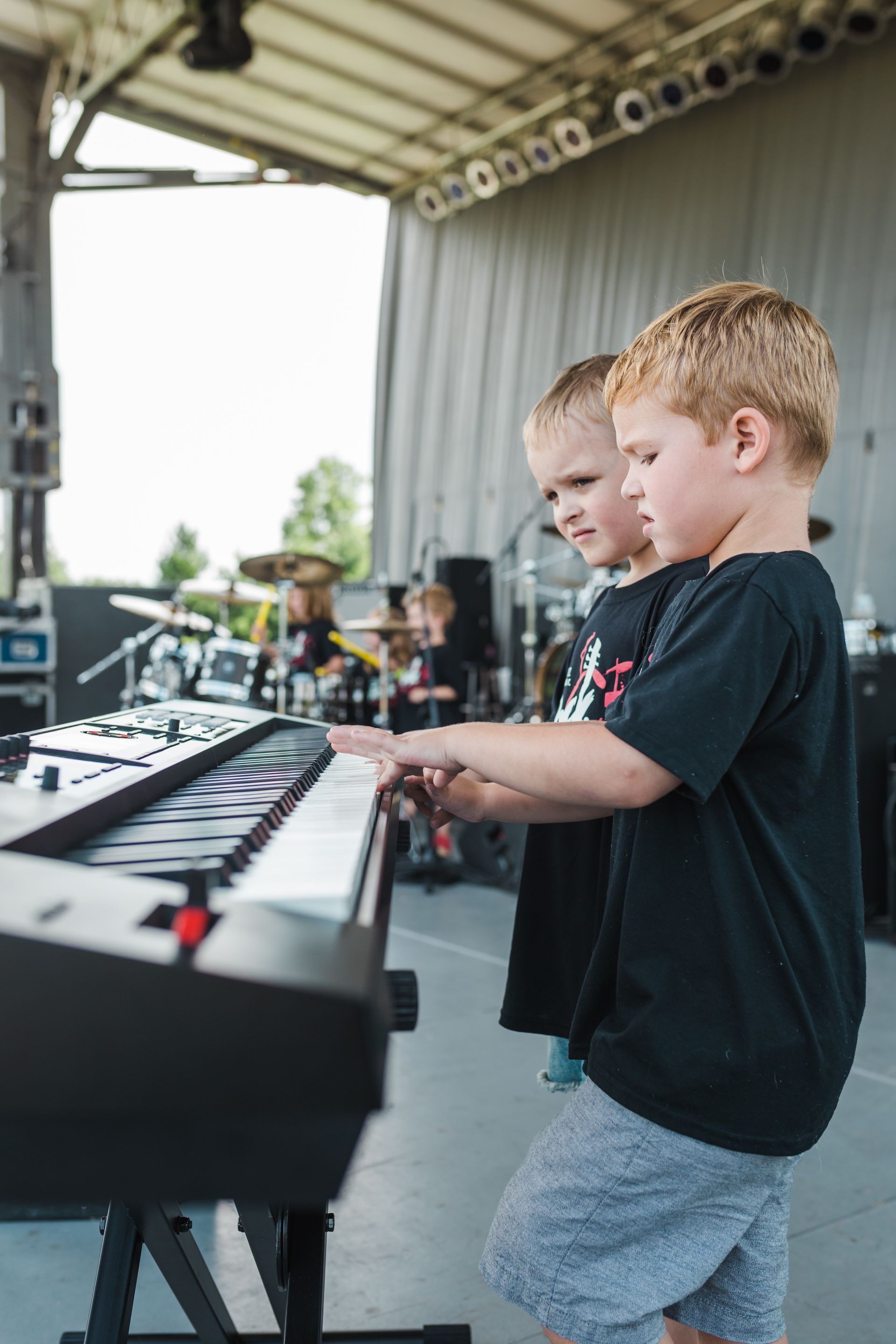 Two young boys are playing a keyboard on a stage.