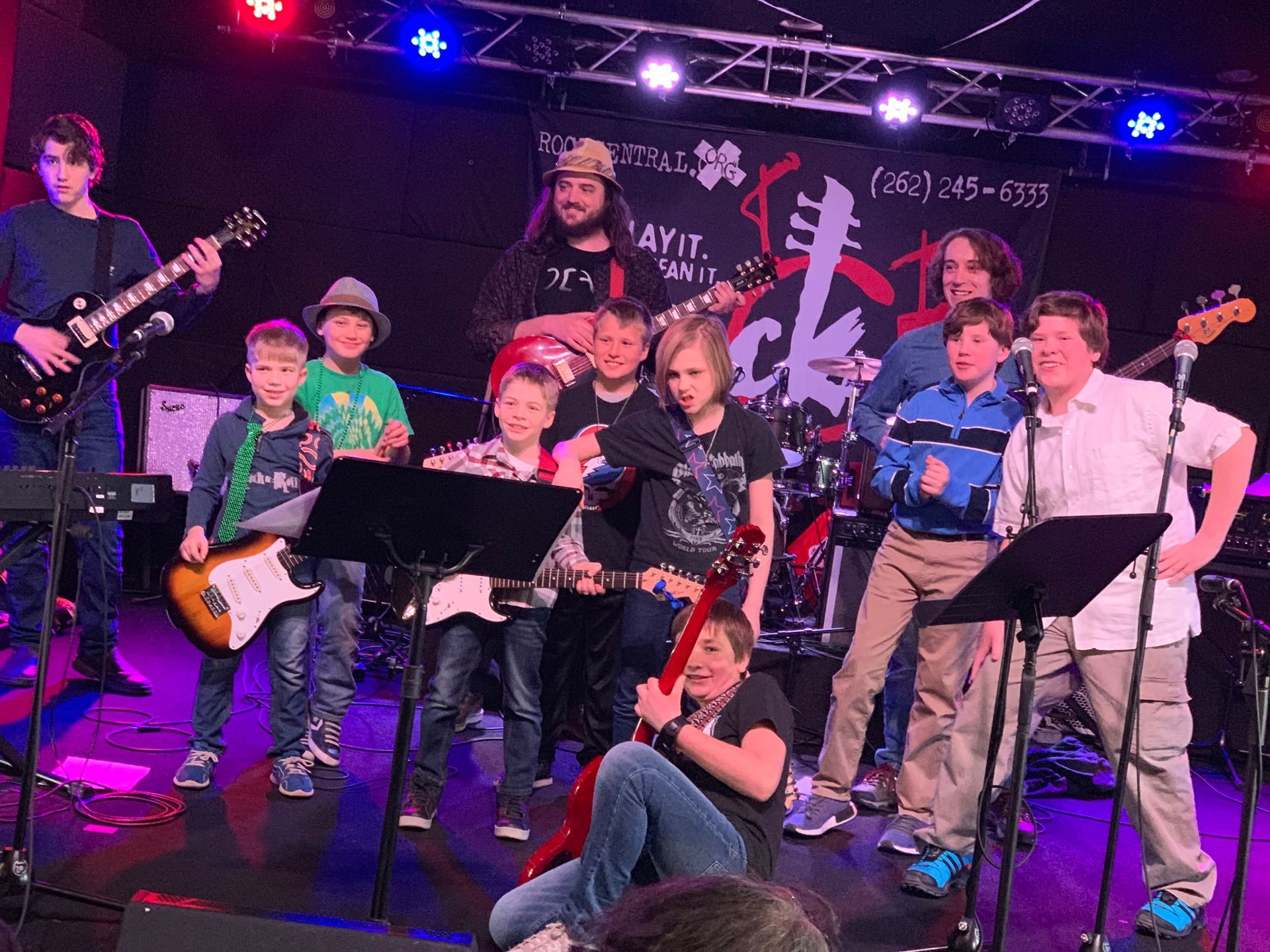 A group of young boys are standing on a stage playing guitars.
