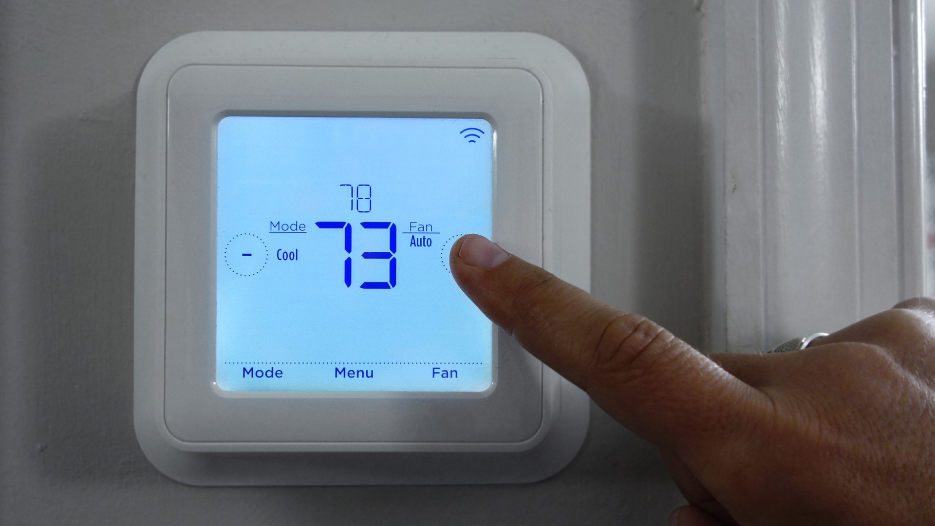 A person is pressing a button on a thermostat.