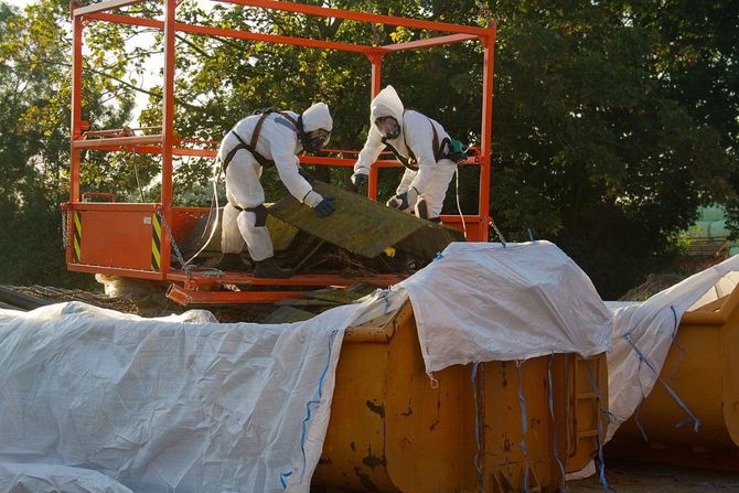 Two workers in white protective suits handling a large bag inside an orange industrial frame outdoors