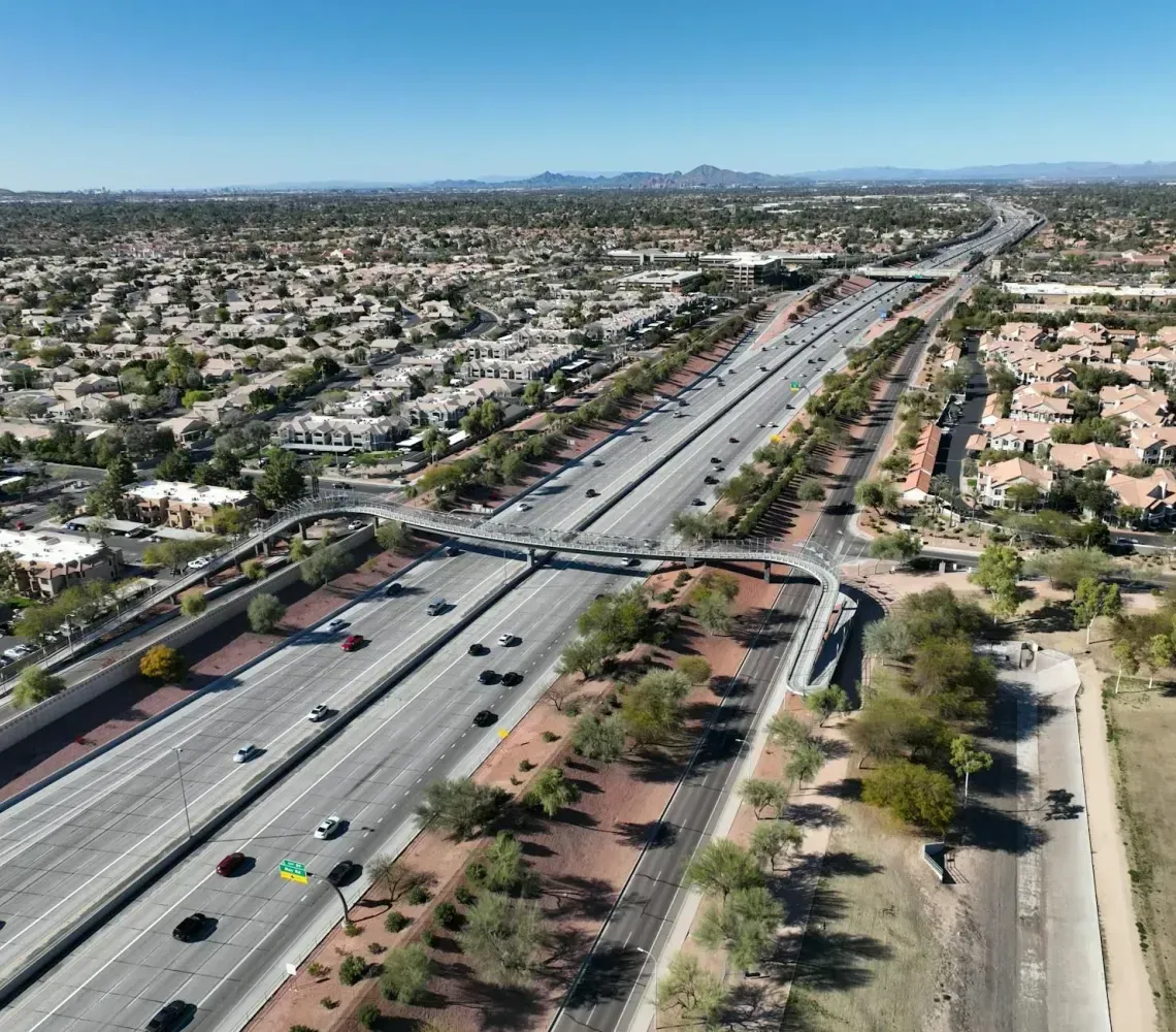 Aerial view of a wide freeway through a sprawling desert suburb with cars and an overpass