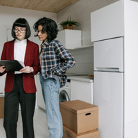 Two people discussing a tablet in a modern kitchen with a white refrigerator and moving boxes.