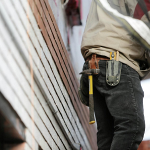 Worker with tool belt standing beside a slanted corrugated metal wall on a construction site