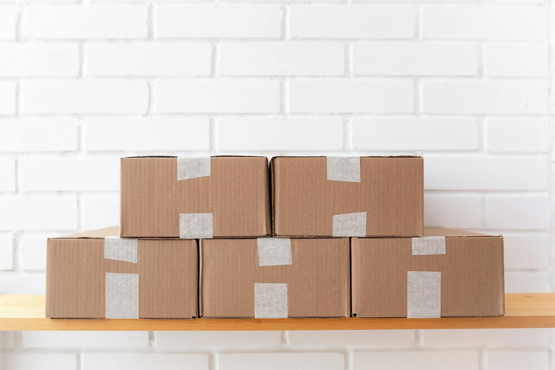Stacked cardboard boxes on a wooden table against a white brick wall